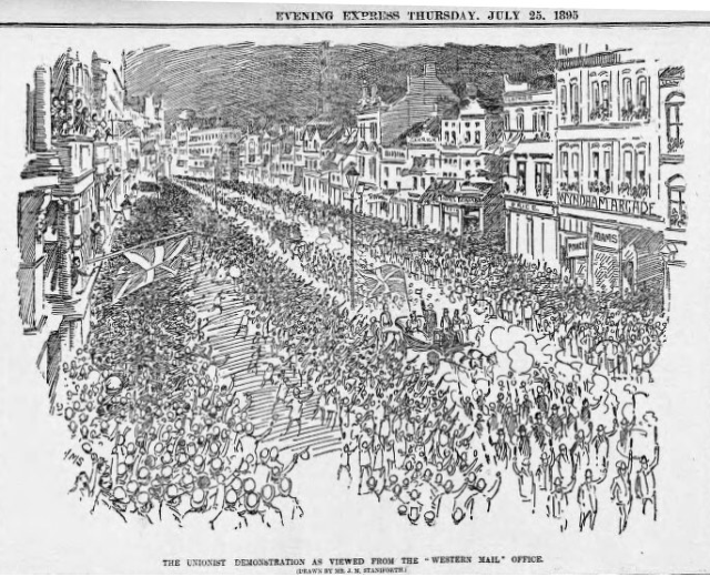 Schwarze und weiße Zeichnung einer Menge, die zwischen Gebäuden die Straße entlanggeht, mit Text oben und unten: "Die Unionistendemonstration, wie sie vom Western Mail Office aus gesehen wird."