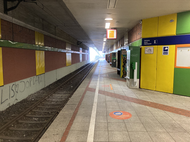Ein Bahnhof in Berlin, Deutschland, mit einem Zug auf den Schienen, beleuchtet von Deckenlampen, Graffiti an der linken Wand und ein paar Gegenständen auf der rechten Seite.