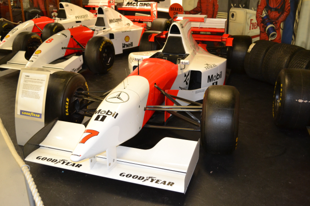 Rennwagen im Museum mit Zuschauern, Texttafel und Absperrseil an einer Wand.