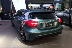 Ein Mercedes-Benz A-Klasse Hatchback auf der IAA in Frankfurt, ein schlankes, modernes Design mit glänzender schwarzer Lackierung, Chromakzenten, sportlichem Look, niedriger Profil, breiter Stand, markantem Kühlergrill und Aluminiumrädern, umgeben von einer Gruppe von Menschen.