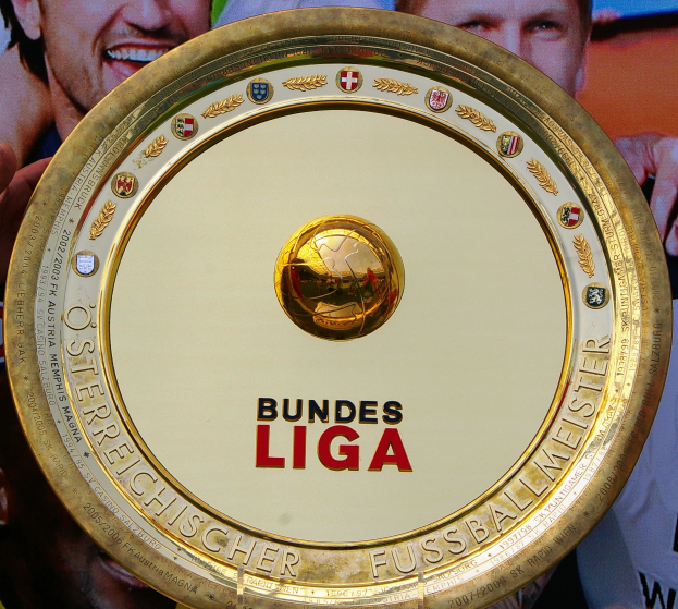 Goldener Schild mit "Bundesliga"-Text in der Hand eines Mannes, mit einem Banner im Hintergrund mit drei Personen