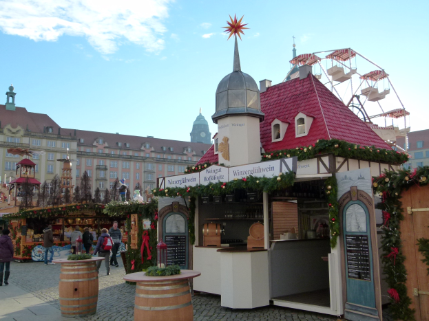Ein geschäftiger Weihnachtsmarkt in Nürnberg, Deutschland mit Menschen um dekorierte Stände, festliche Lichter, ein Riesenrad im Hintergrund und ein Schild rechts.