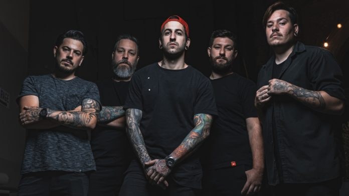 Eine Gruppe von Männern, die in einem dunklen Raum während eines Interviews stehen, von rechts beleuchtet, wahrscheinlich für Avenged Sevenfold.