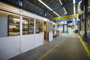 Großes Lagerinneres mit zahlreichen Fenstern, Türen, Tischen, Rohren, Lampen und anderen industriellen Objekten.