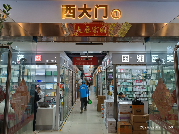 Innenansicht einer chinesischen Apotheke mit Glaswänden, einer Pflanze links, Regalen voller Artikel, verstreuten Kartons und Gegenständen auf dem Boden und einem Namensschild oben, das darauf hinweist, dass es ein chinesischer Drogeriemarkt ist.