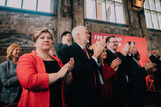 Gruppe von Menschen, die vor einer Menge jubeln, mit einem Banner im Hintergrund, auf dem Wahlsieg steht.