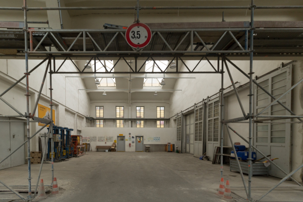 Lagerhalle mit Gerüst, Verkehrszeichen, Metallstangen, einem Schild, Maschinen, einer Tür, Fenstern, einer Wand, Deckenleuchten und einem Dach.