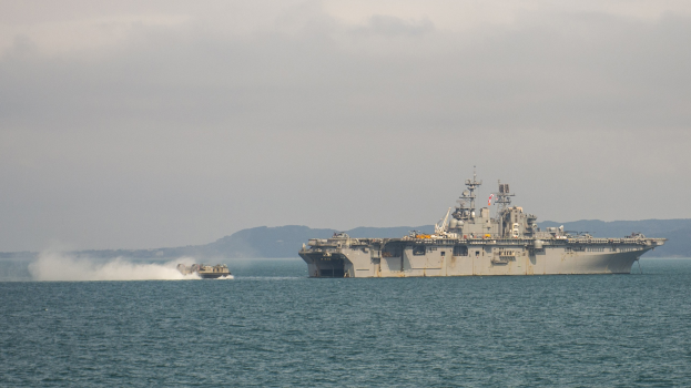 USS George H W Bush Flugzeugträger CVN-68 durchquert den Straße von Hormuz mit zwei Booten im Vordergrund und Bergen und Wolken im Hintergrund.
