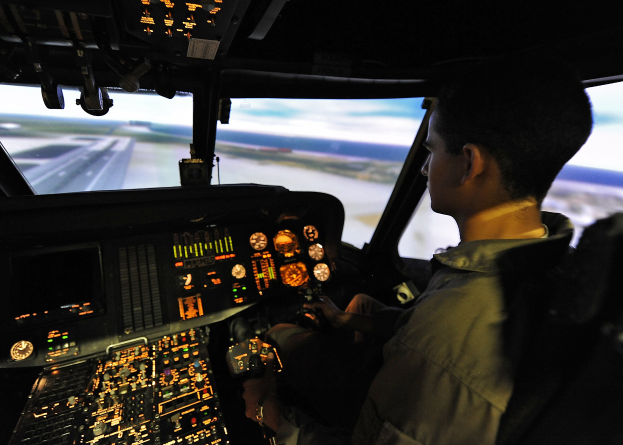Ein Mann sitzt im Cockpit eines Flugzeugsimulators und blickt aus dem Fenster auf die Start- und Landebahn und den Himmel. Er ist von Anzeigegeräten und Steuerungen umgeben.