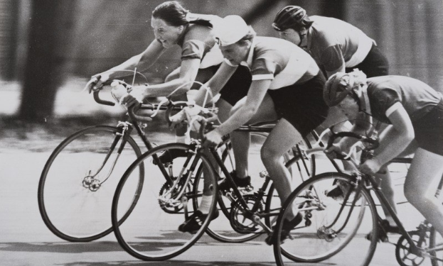 Eine Gruppe von Frauen in Helmen auf Fahrrädern auf einer Straße in einem Schwarz-Weiß-Foto