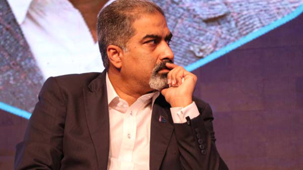 Ein Mann in Anzug und Krawatte sitzt auf einer Bühne und sieht konzentriert auf einen Bildschirm.