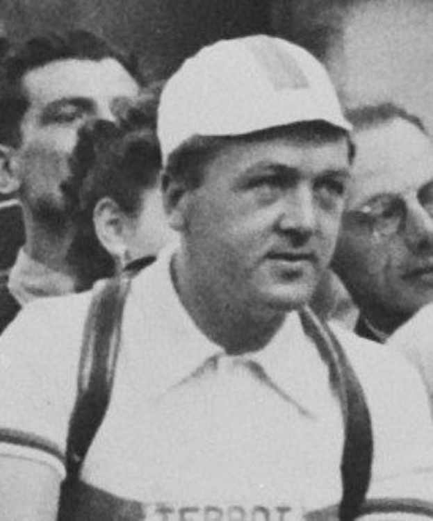 Schwarzes und weißes Foto eines Mannes mit Mütze und Hosenträgern, der vor einer Gruppe von Menschen steht und mutmaßlich ein legendärer Fußballspieler ist.