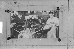 Zwei Männer in einer Fabrik inspizieren ein Flugzeugtriebwerk, aufgenommen in Schwarzweiß.