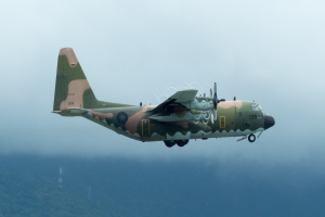 Ein Militärflugzeug fliegt durch einen klaren blauen Himmel und hinterlässt eine Rauchspur.