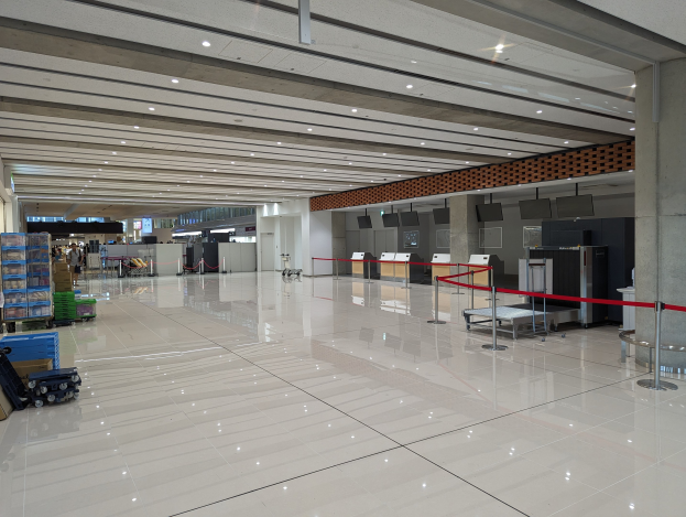 Großer Flughafen-Terminal mit Gepäck, Wägen, Kartons, Absperrpoller mit Bändern, Säulen, wandmontierten Fernsehern und Deckenleuchten, wahrscheinlich ein Check-in-Bereich.