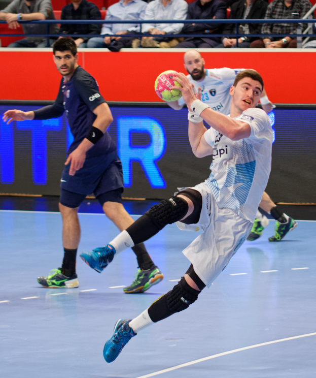 Mannergruppe spielt Handball auf einem Feld während der Futsal-Weltmeisterschaft 2019, mit Zuschauern im Hintergrund.