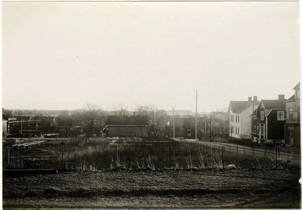 Schwarzes und weißes Foto einer Stadtstraße mit Gebäuden, Pfählen, Bäumen, Pflanzen, einem Zaun im Vordergrund und dem Himmel im Hintergrund, das die Baustelle einer neuen Wohnsiedlung in St. Louis, Missouri, zeigt.