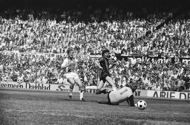 Schwarzes Foto von Männern, die auf einem Feld Fürball spielen, mit Zuschauern im Hintergrund und einer "Bundesliga 1978-79 Ajax 1-1 Hannover 96"-Fahne.