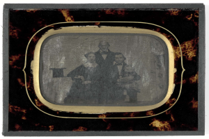 Schwarz-weiß-Foto eines Mannes im Anzug und einer Frau in unbekannter Kleidung, die vor einem alten Fernseher stehen und ernst schauen.