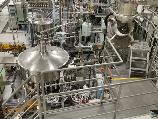 Eine große Reaktor-Maschine in einem Gebäude, umgeben von verschiedenen Komponenten und Maschinen, mit einem Boden, Geländern und Treppen.