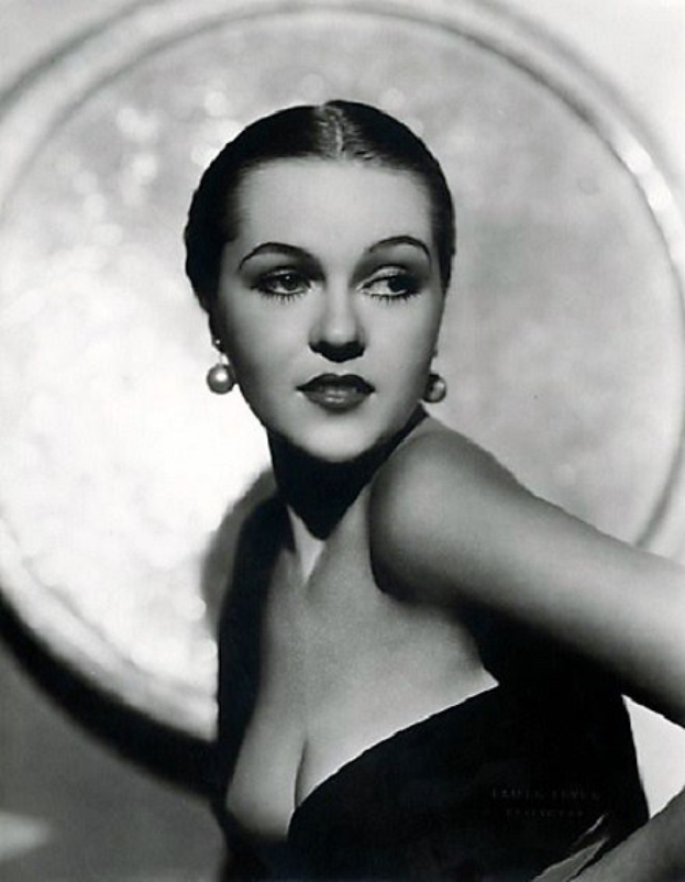 Schwarz-weiß-Porträt einer Frau in einem langärmligen, hochgeschlossenen Kleid mit 1940er-Jahre-Stil und Make-up, die direkt in die Kamera schaut.