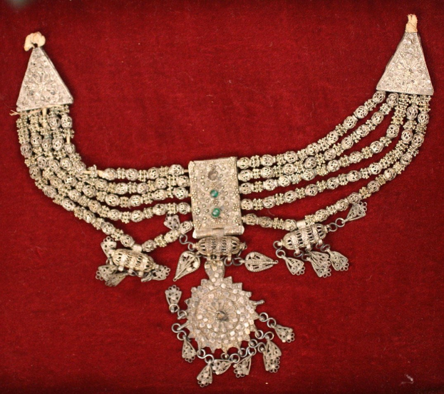 Silberne Halskette mit Smaragden und Diamanten auf rotem Samt-Hintergrund.