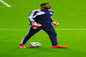 Ein Mann in einem Fußballtrikot steht auf einem Feld und hält einen Fußball.