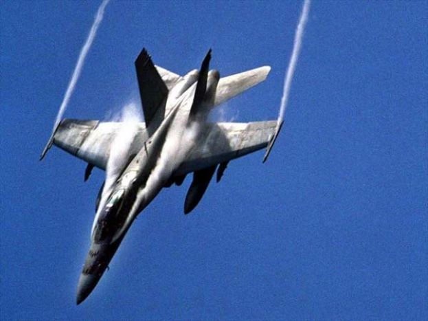 Kampfjet fliegt durch einen hellblauen Himmel mit einer Rauchspur hinter sich, unten ist Text sichtbar.