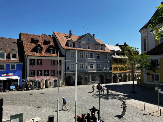 Eine Gruppe von Menschen, die Fahrräder auf einer Kopfsteinpflasterstraße in der Altstadt von Heidelberg, Deutschland, fahren, mit Gebäuden, Laternenpfählen, Bäumen, Bänken und Himmel im Hintergrund.