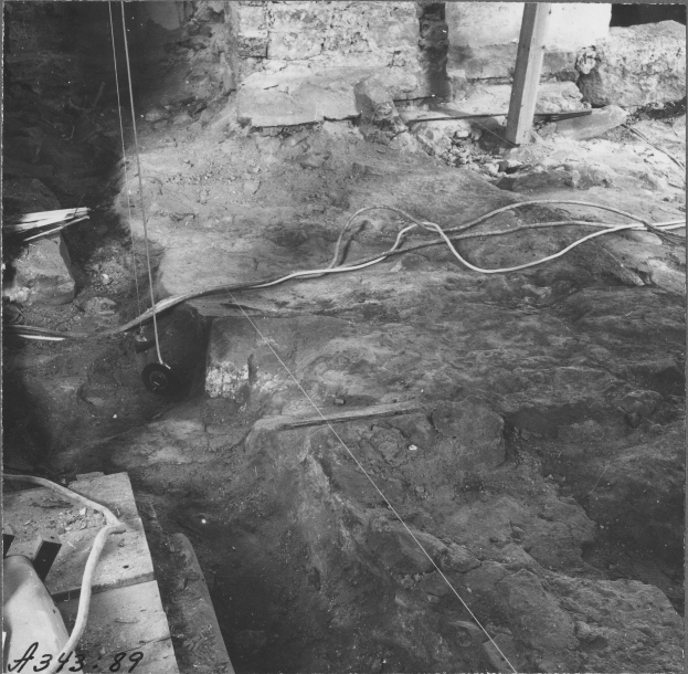 Ein Schwarz-Weiß-Foto eines Grabens mit einem Rohr darin, umgeben von Steinen, hölzernen Gegenständen und einer Wand, mit Text unten.