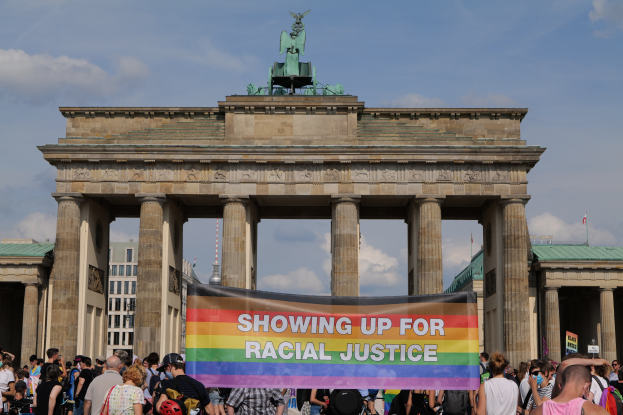 Eine Gruppe von Menschen mit einem "Rassengerechtigkeit"-Schild vor dem Reichstagsgebäude in Berlin, mit den Säulen und der Statue des Gebäudes im Hintergrund und Gebäuden und bewölktem Himmel.