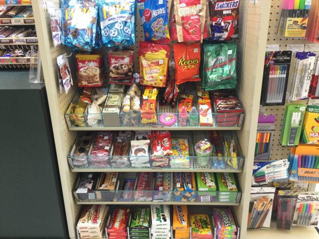 Ladeninneneinrichtung mit verschiedenen Süßwarenprodukten auf Regalen und Gestellen, darunter Packungen, Schachteln und Stifte, mit einem Süßwaren-Display auf der linken Seite.