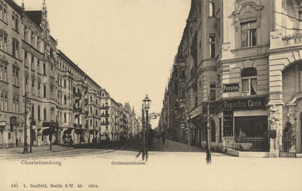 Schwarz-weiß-Foto einer Stadtstraße in Charlottenburg, Deutschland, mit Gebäuden, Straßenlaternen, Schildern, Fahrzeugen, Fußgängern, Gittern und einem klaren Himmel.