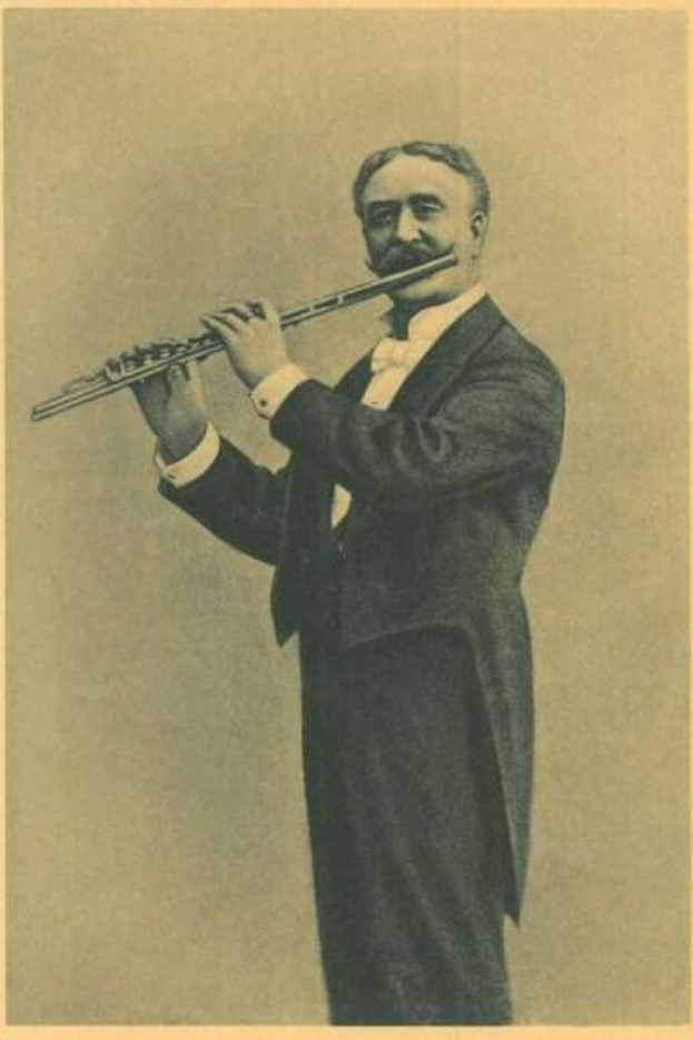 Ein Schwarz-Weiß-Foto eines Mannes in einem Smoking, der auf der Bühne eine Flöte spielt, die Augen geschlossen und konzentriert, mit zurückgekämmtem Haar und beleuchtet von der Bühnenbeleuchtung.