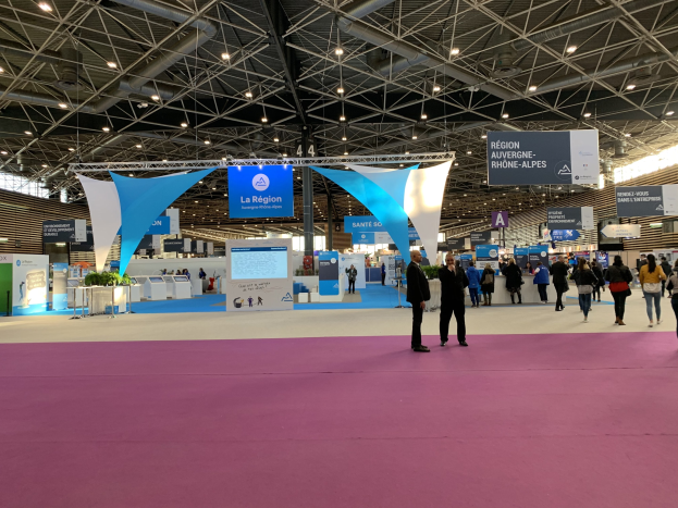 Ein großer Messestand mit Menschen, die herumlaufen, einige tragen Taschen, unter beleuchteten Bannern und Tischen mit Ausstellungsstücken, wahrscheinlich von der Pariser Internationalen Handelsmesse 2018.