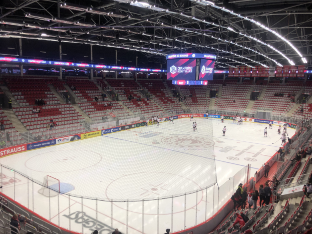 Eishockeyspiel in einer großen Arena zwischen den St. Louis Blues und den Detroit Red Wings, mit Zuschauern auf den Sitzplätzen und Stehplätzen in der Nähe der Eisfläche, umgeben von einem Zaun und Metallrahmen, unter einer Dachkonstruktion mit Deckenleuchten und einem Display.