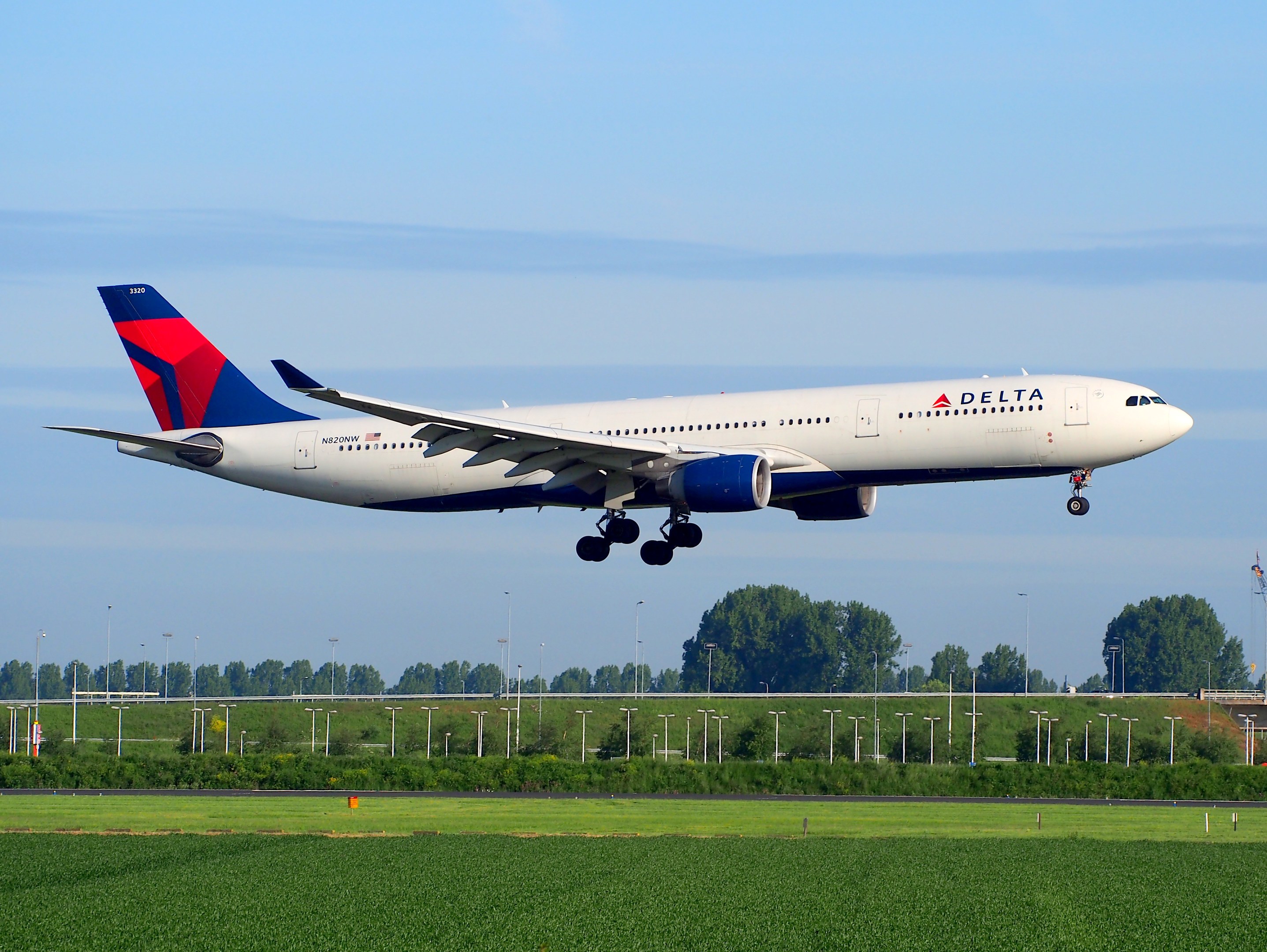 Ein Delta Air Lines Boeing 787-9 Dreamliner startet von Frankfurt Airport, mit grünem Gras, Laternenpfählen, Bäumen, einem Turm auf der rechten Seite und einer bewölkten Himmel.