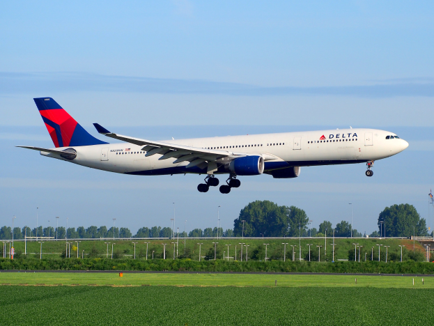 Ein Delta Air Lines Boeing 787-9 Dreamliner startet von Frankfurt Airport, mit grünem Gras, Laternenpfählen, Bäumen, einem Turm auf der rechten Seite und einer bewölkten Himmel.