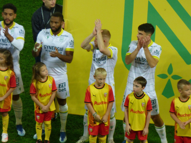 Eine Gruppe junger Fußballspieler in Uniformen klatscht auf einem Ligue-1-Feld in Feierlaune, mit einem "Ligue-1"-Schild im Hintergrund.