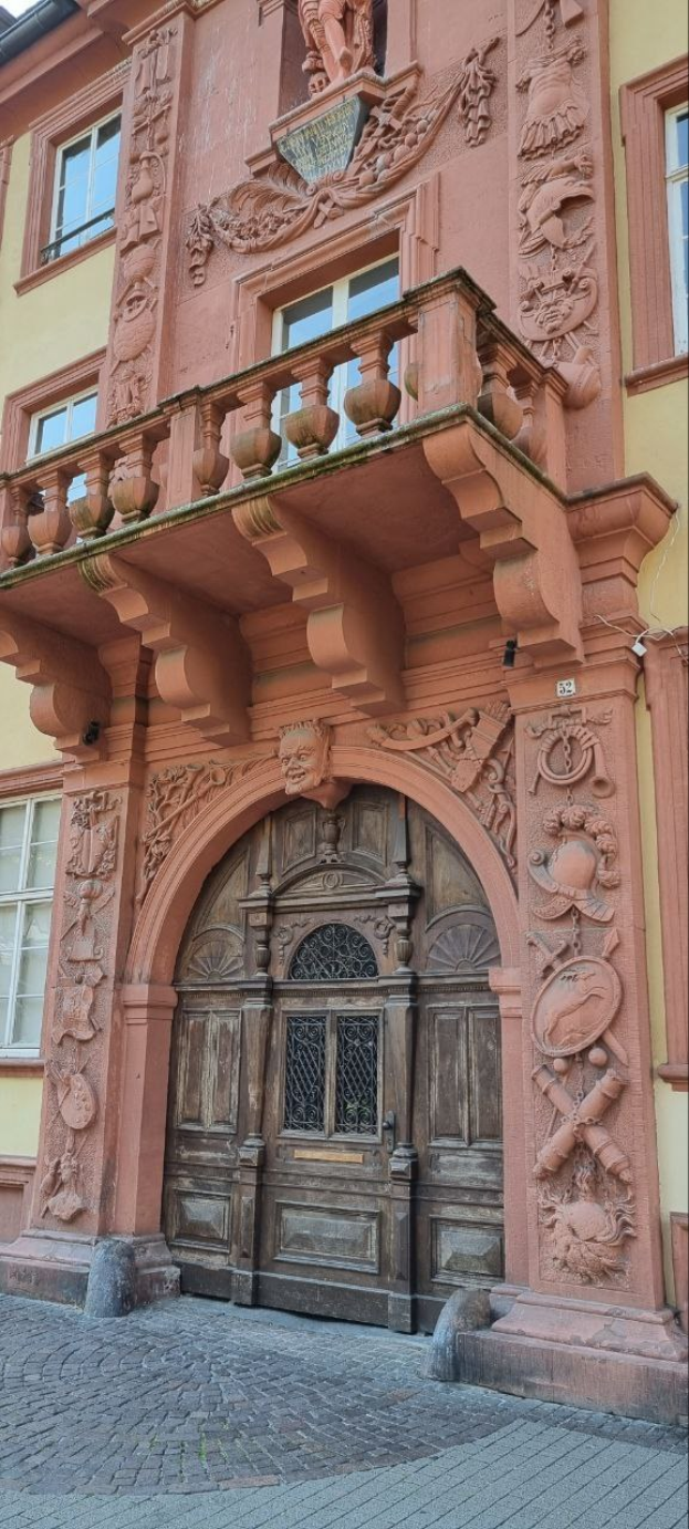 Ein altes Gebäude in Heidelberg, Deutschland, mit einer hölzernen Tür, Fenstern und detaillierten Schnitzereien an seiner Fassade.