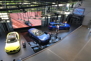 Eine Gruppe von Menschen steht im BMW Museum in München, links sind Autos ausgestellt und rechts ein Schild mit der Aufschrift "BMW Museum München".