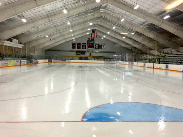 Große Indoor-Eisfläche mit Deckenbeleuchtung, Werbetafeln, Treppen mit Geländern und wenigen Personen, was auf eine Sportanlage hinweist, die wahrscheinlich für Hockey genutzt wird.