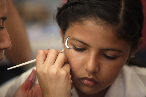 Ein junges Mädchen sitzt, während ein Make-up-Artist ihr Make-up mit einem Pinsel aufträgt, mit einem unscharfen Hintergrund.