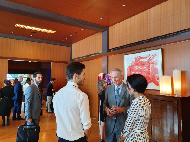 Menschen, die in einem Raum mit einer hölzernen Wand mit einem Fotorahmen und Lampen stehen und sich unterhalten, wobei einige Taschen tragen, auf einer von der Nationalgalerie Singapore veranstalteten Kunstmesse.