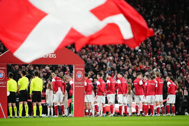 Gruppe von Menschen auf einem Fußballfeld mit einer roten und weißen Flagge im Vordergrund, einem Bogen mit "Bayern Munich vs. Bayern Munich Wett-Tipps & Vorschau"-Text im Hintergrund und einer großen Menge im Stadion.