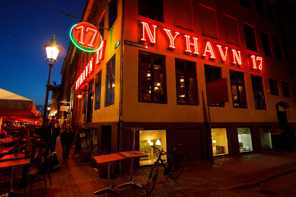 Ein Gebäude mit rotem Text darauf, ein Fahrrad und Tische und Stühle daneben, mit einer Straßenansicht im Hintergrund.