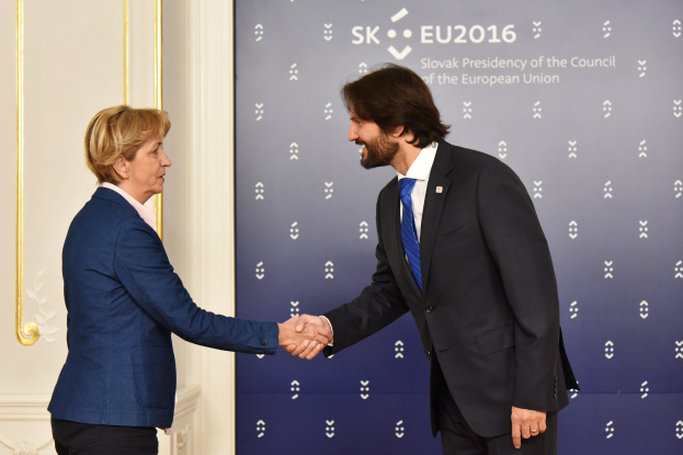 Bundeskanzlerin Angela Merkel und Bundespräsident Joachim Gauck schütteln sich die Hände und lächeln bei einem EU-Gipfeltreffen, mit einem "EU-Gipfeltreffen"-Banner und einer Tür im Hintergrund.