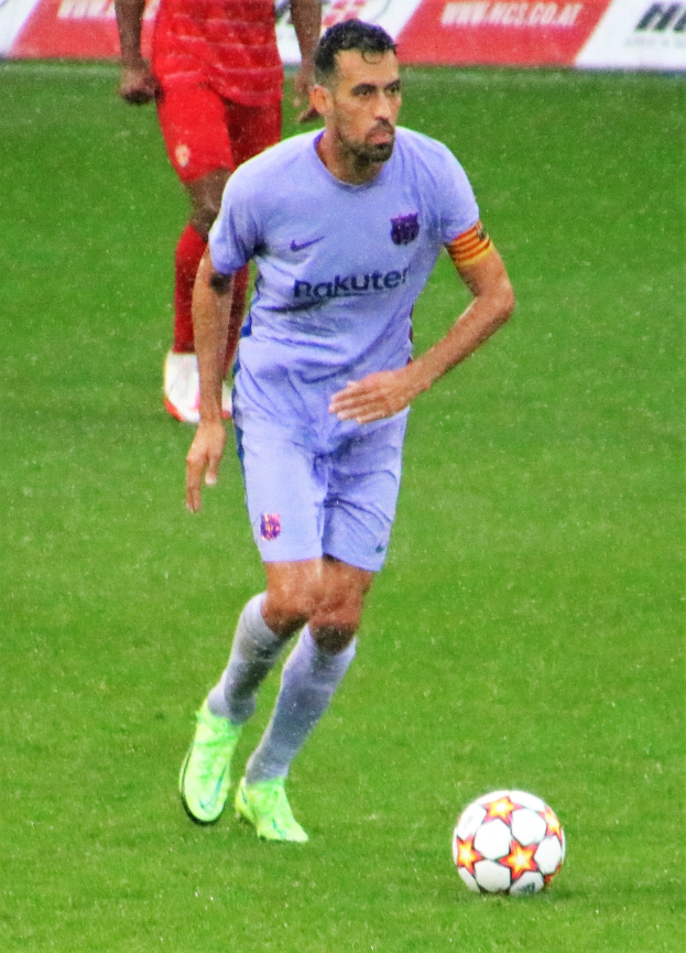 Ein Fußballspieler in Sportbekleidung und -schuhen auf dem Feld mit einer Texttafel im Hintergrund.
