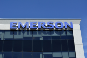 Das Emerson-Logo an der Seite eines Geb├Ąudes mit dem Text "Emerson investiert $1,5 Milliarden in den USA" vor einem klaren blauen Himmel.