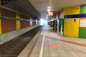 Ein Bahnhofsgebäude in Berlin, Deutschland, mit einem Zug auf den Gleisen, beleuchteter Deckenbeleuchtung, Graffiti an der linken Wand und einigen Gegenständen auf der rechten Seite.